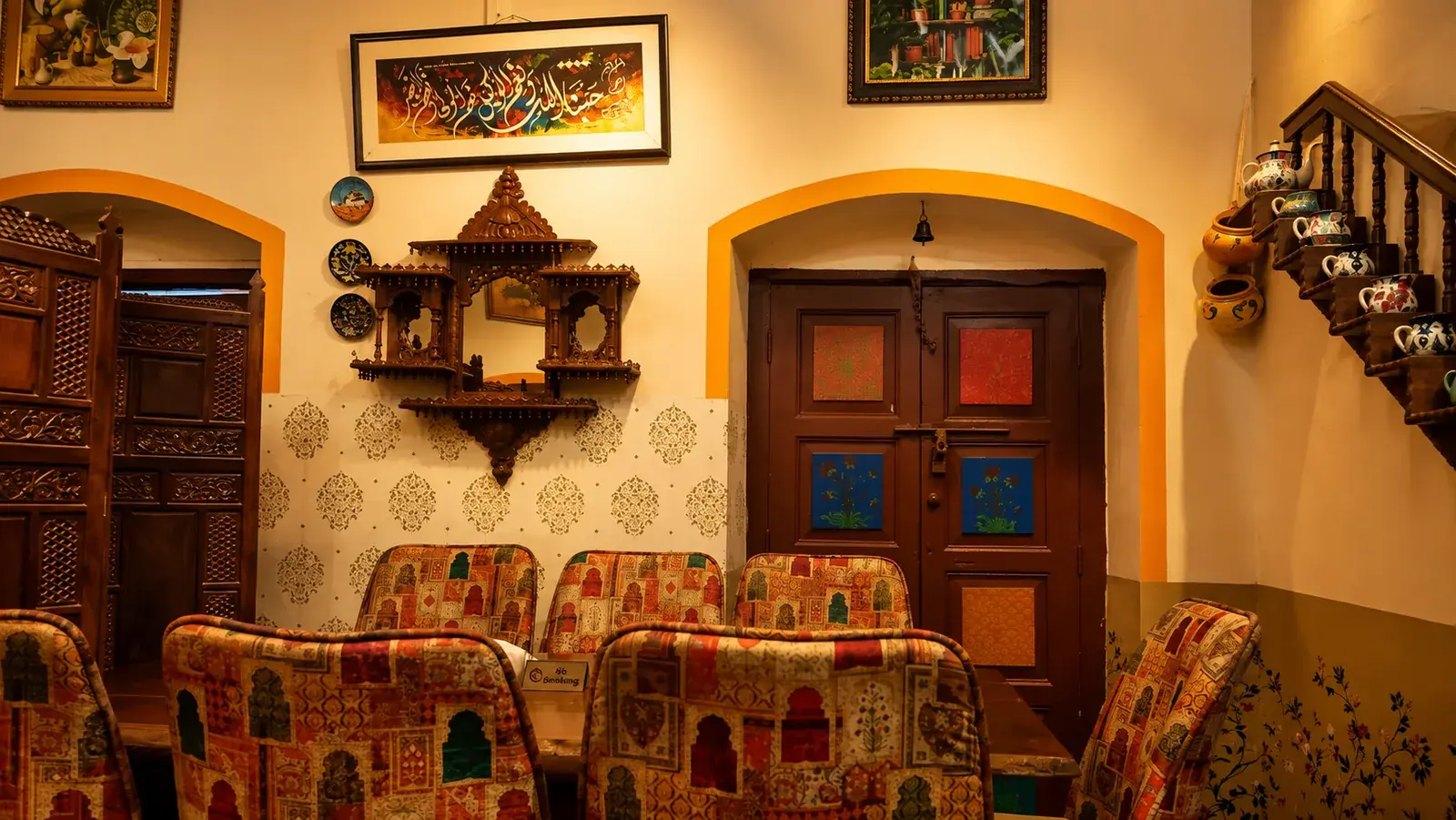 Carved seating beneath the staircase, mirror and red doors behind